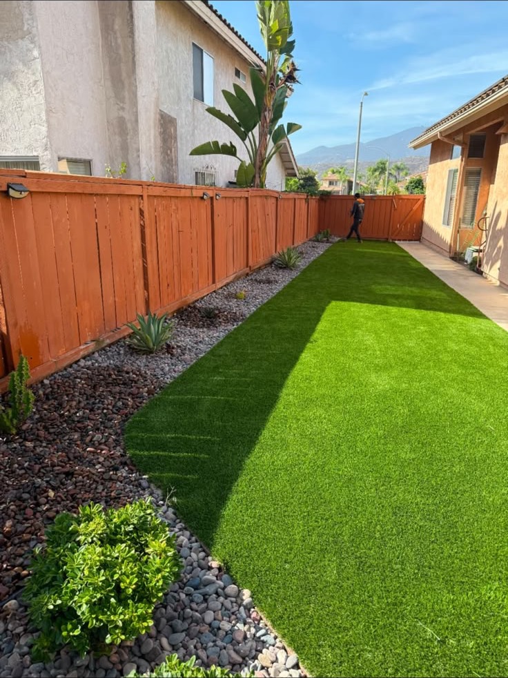 Completed side-yard landscape with turf, river rock, planting, and a clean edge